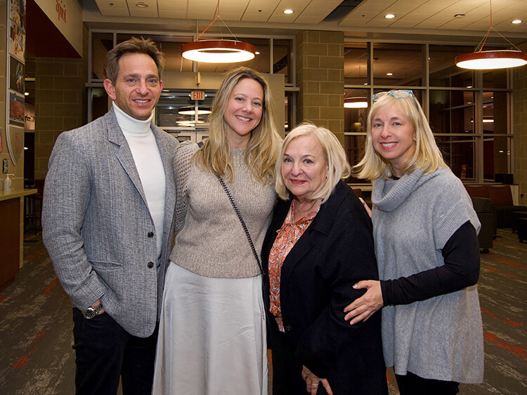 The Plotkin Family smiling indoors. The room has warm lighting and modern decor. Everyone appears relaxed and happy, conveying a sense of togetherness.